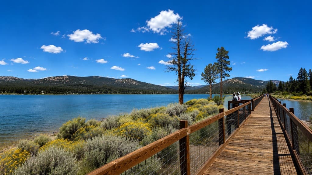Wooden boardwalk along a mountain lake, with forested hills across the water.